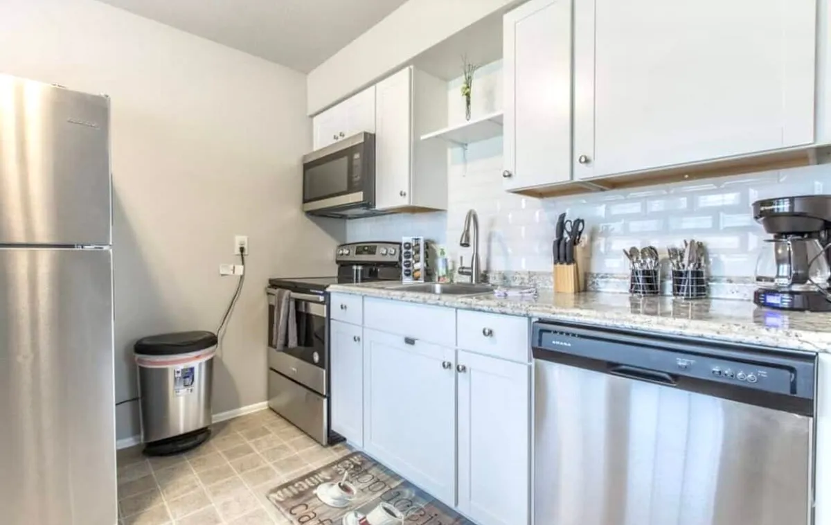 A modern kitchen featuring stainless steel appliances, a granite countertop, sleek modern cabinets, and various kitchen utensils. The space is bright and inviting, clearly designed with meal preparation and entertaining in mind.