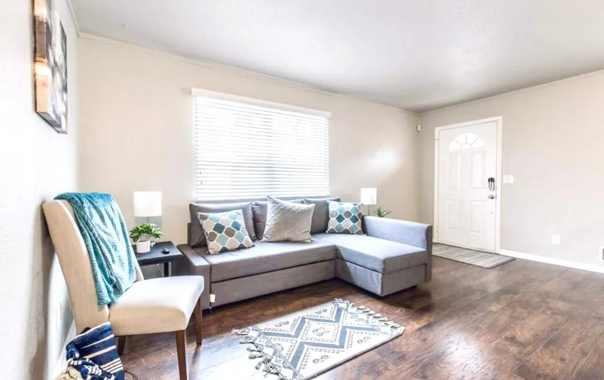 The scene captures another angle of a cozy living space, featuring a comfortable sofa with decorative pillows, a stylish chair, and an area rug that ties the room together. A doorway in the background hints at easy access to other areas, suggesting a flexible, open environment for work or relaxation.