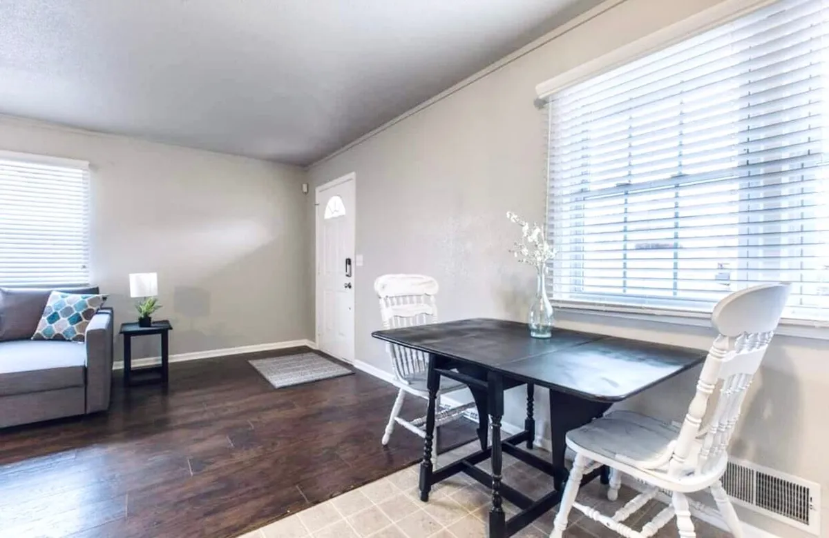 The image shows an inviting interior where a comfortable sofa, a dining table set near a window, and a door leading to another part of the home share the space. The setting is casual yet welcoming, perfect for family dining or relaxed socializing.