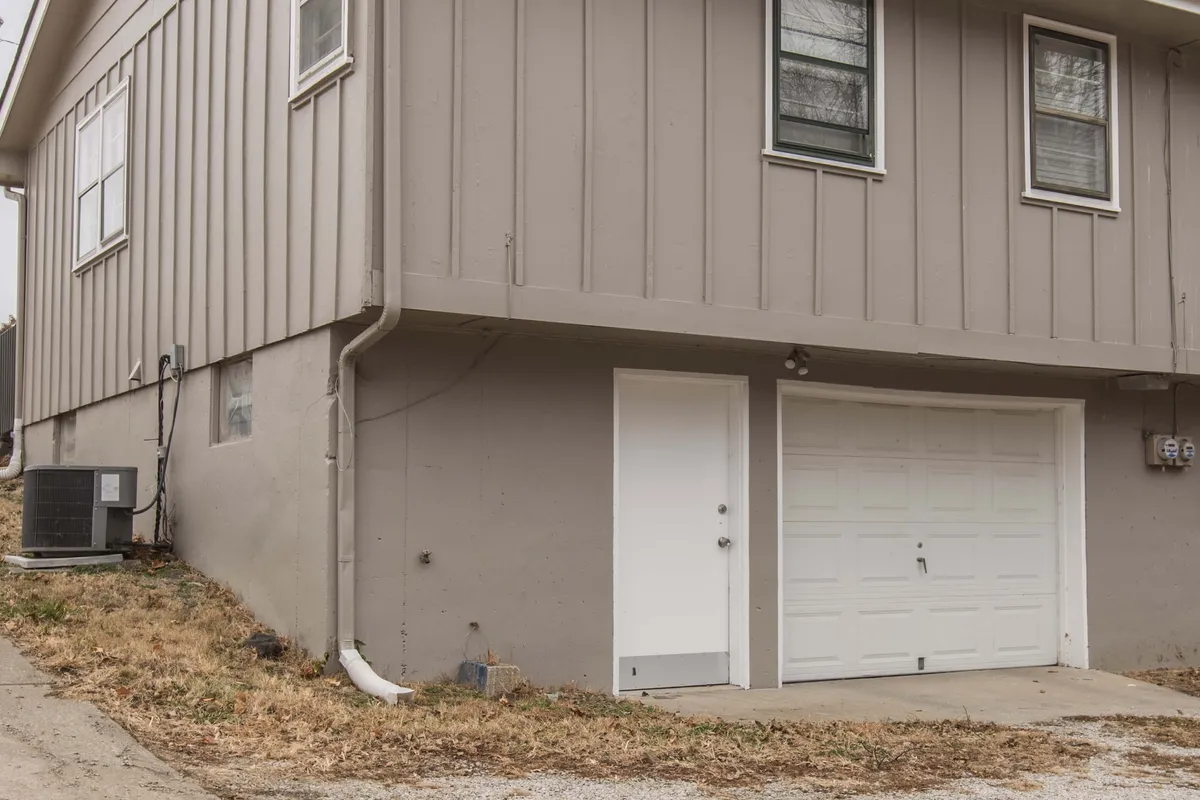 An exterior view of the home's garage door, side entrance, and windows. The setting suggests a welcoming environment for families returning from a day out, with visible areas where kids might play in the yard and where families can gather outdoors.